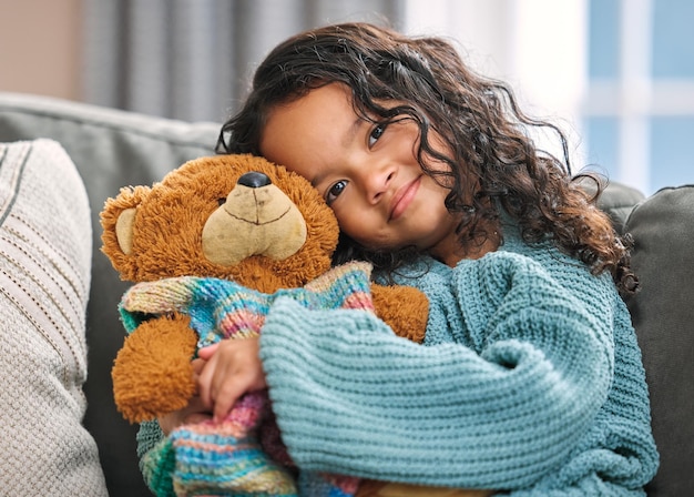 This is my favourite teddy. Shot of an adorable little girl sitting alone on the sofa at home and holding a teddy bear.