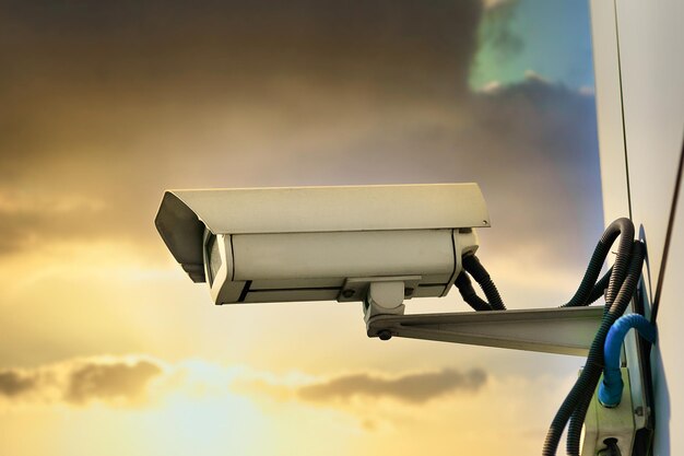 This is a security camera hanging on the wall of a building\
against the backdrop of a dramatic sunset