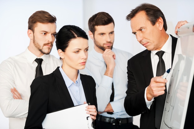 This is very important! Confident mature businessman pointing a graph on whiteboard while his colleagues standing near him and looking at sketch