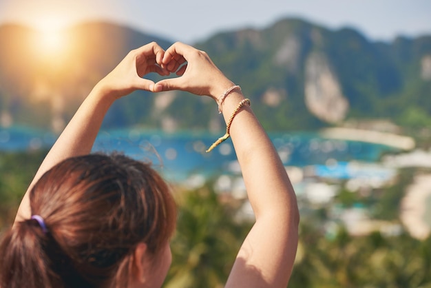 This island has stolen her heart Rearview shot of a happy young tourist making a heart with her hands against a beautiful landscape