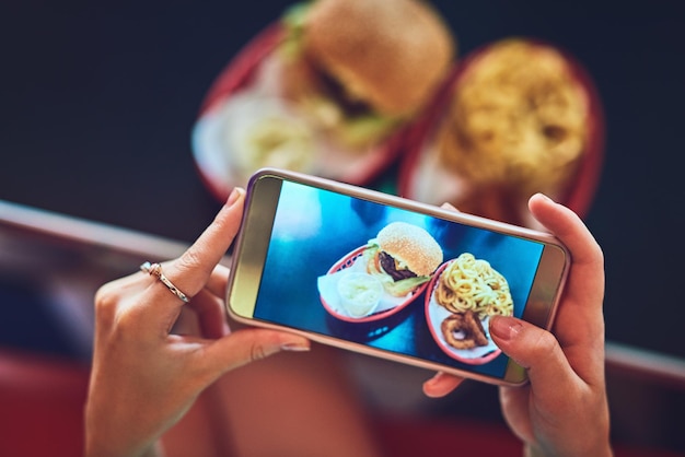 Questo è online inquadratura dall'alto di una giovane donna irriconoscibile che scatta foto del suo hamburger in una tavola calda retrò