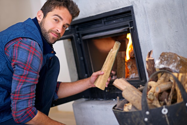 Photo this should warm things up shot of a young man building a fire in his fireplace at home