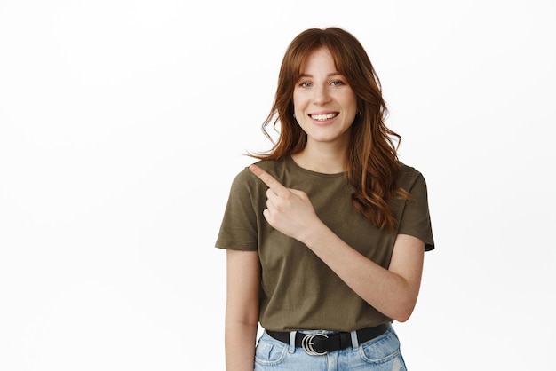 This way Smiling cute girl student pointing at upper left corner showing advertisement or banner on empty space standing against white background