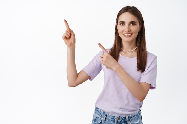 Per di qua. ragazza sorridente amichevole che punta a sinistra, mostrando pubblicità, direzione al banner o testo promozionale contro uno spazio bianco vuoto, sfondo dello studio