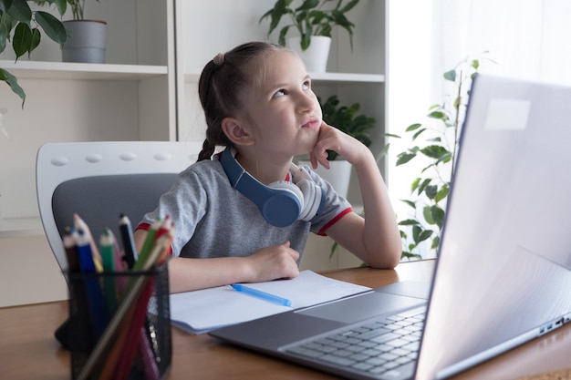 Thoughtful 6-8 year old girl studying at the computer does
homework communicates on the internet.