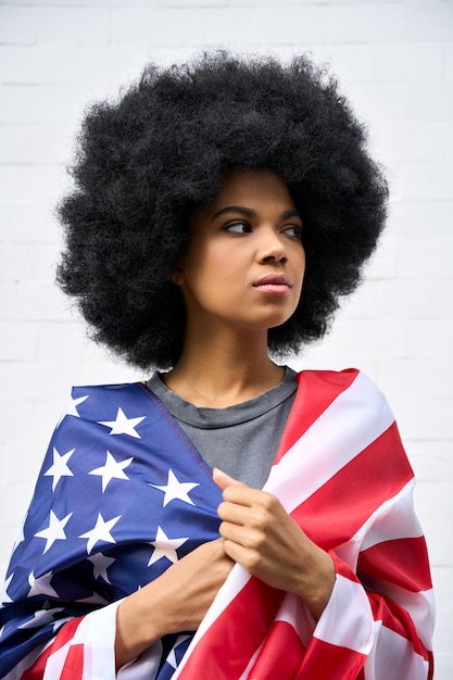 Thoughtful Afro American girl wrapped in usa flag standing on white background