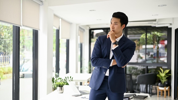 Thoughtful Asian businessman in formal business suit hand on chin looking out the window