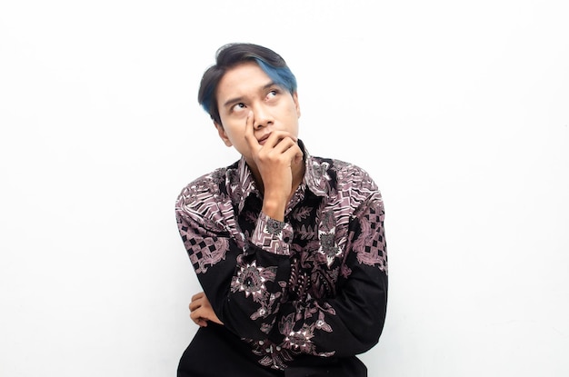 A thoughtful asian man with peek a boo blue hair wearing batik shirt is thinking and wondering.