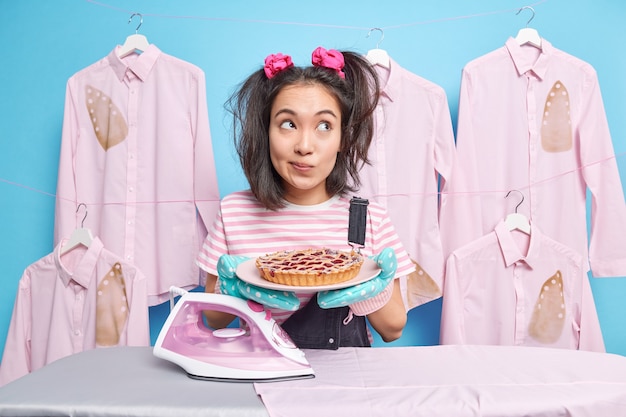 Thoughtful Asian woman housekeeper with two pigtails holds plate of tasty baked pie