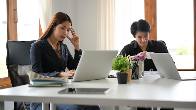 オフィスで彼女のポータブルラップトップコンピューターに取り組んでいる思いやりのあるアジアの若い実業家