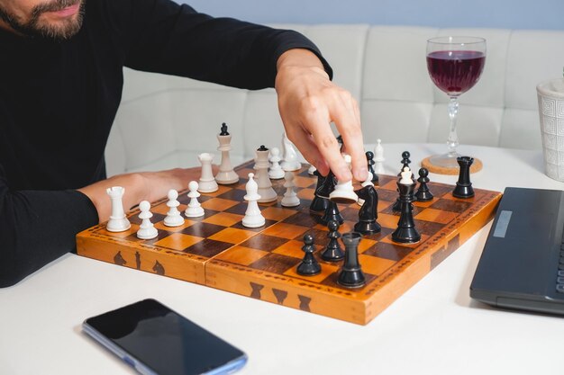 Thoughtful bald man wearing beard playing chess on board near\
laptop and wineglass