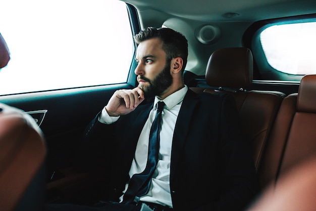 Thoughtful bearded Businessman in taxi cab looking by car window