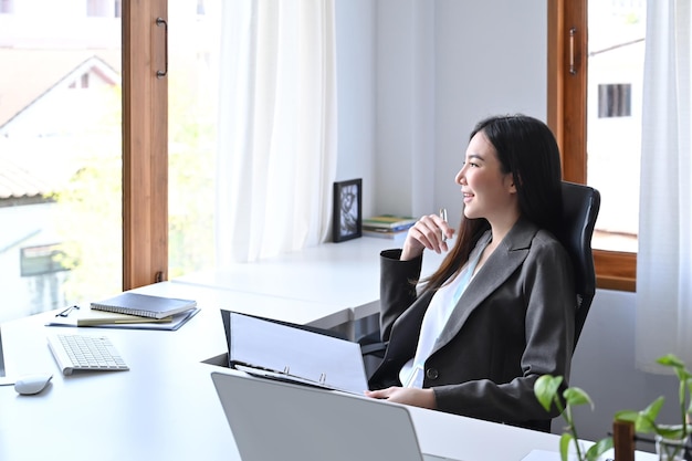 Thoughtful beautiful businesswoman sitting at her workplace and looking out of window.