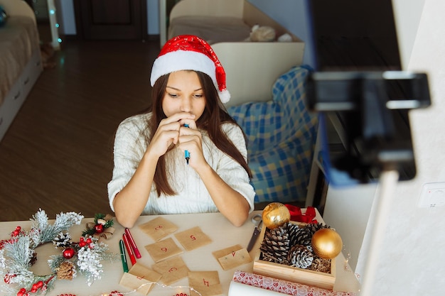 thoughtful blogger girl in a Christmas hat in front of a table with Christmas crafts