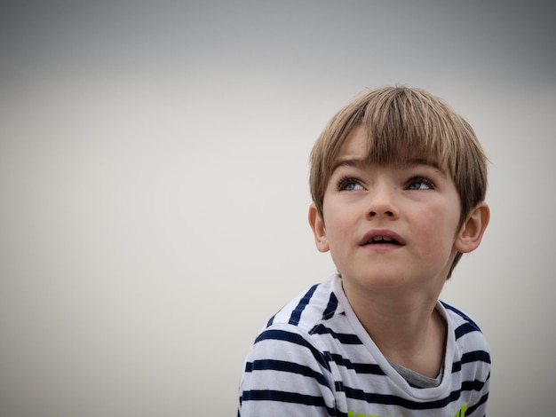 thoughtful boy looking away while sitting against gray background