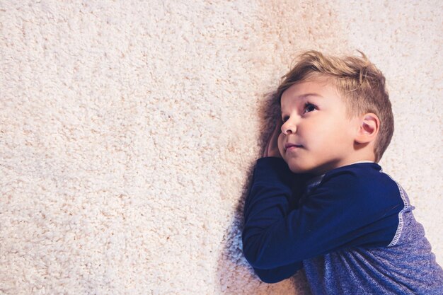 Thoughtful boy lying on rug at home