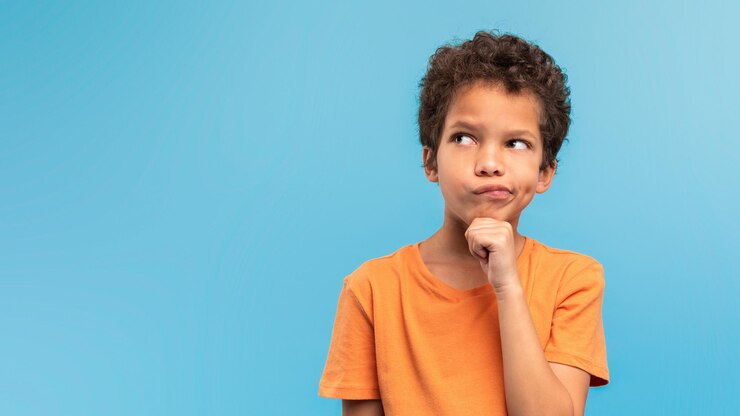Photo thoughtful boy in orange pondering on blue background free space