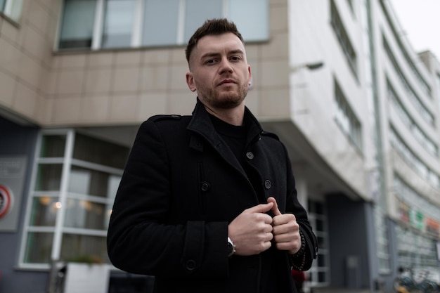 Thoughtful brutal man in a stylish coat on the background of the building