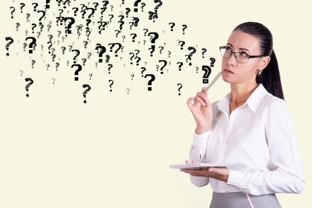 Thoughtful business woman in glasses against the background of a wall with question marks. Decision and doubt concept. Copy space. High quality photo