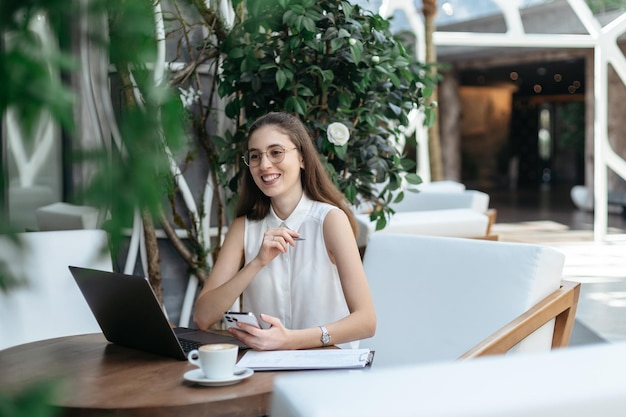 Thoughtful business woman sitting in front of an open laptop in a cafe