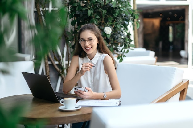 Thoughtful business woman sitting in front of an open laptop in a cafe