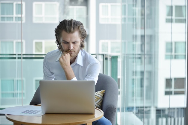 Photo thoughtful businessman using laptop while sitting at office