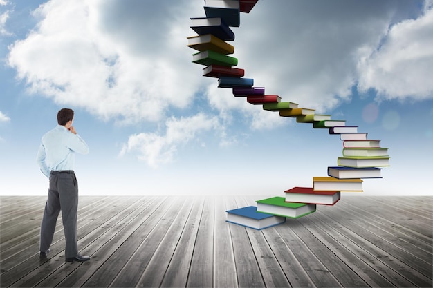 Thoughtful businessman with hand on chin against book steps against sky