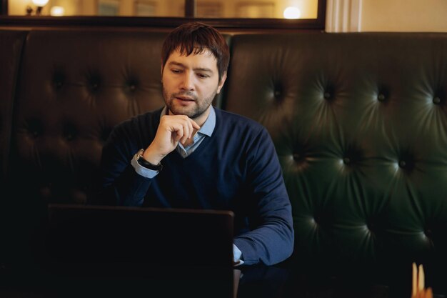 Thoughtful businessman working on new online project on laptop computer sitting at the table in cafe Instant workplace