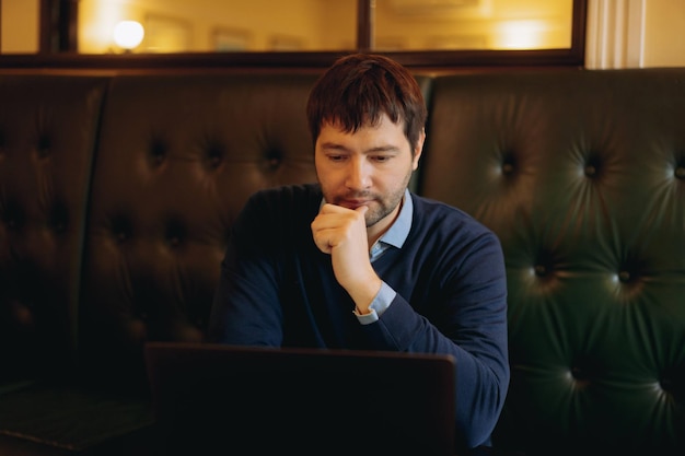 Thoughtful businessman working on new online project on laptop computer sitting at the table in cafe Instant workplace