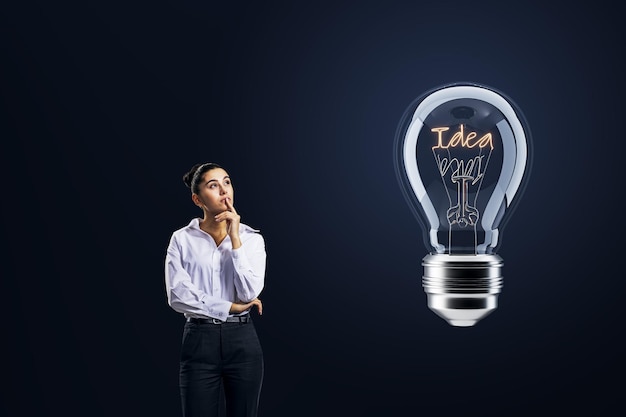 Thoughtful businesswoman looking at light bulb on dark background Idea concept