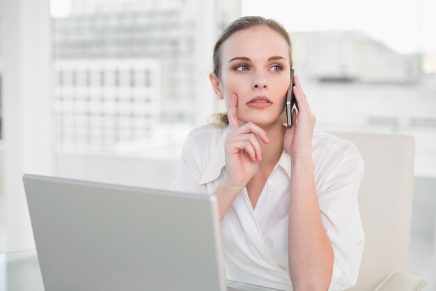 Thoughtful businesswoman using laptop and making a call