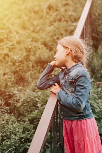 Thoughtful candid eight year old kid girl stands on staircase with grass and enjoying nature prepubertal age of children and their lives mind psychology and mental health concept flare