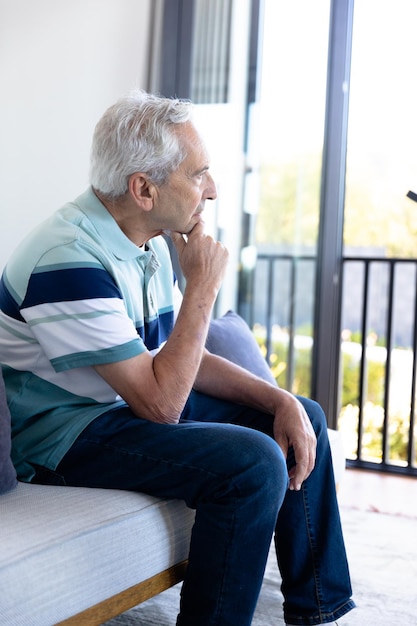 Thoughtful caucasian senior man looking out of the window at home