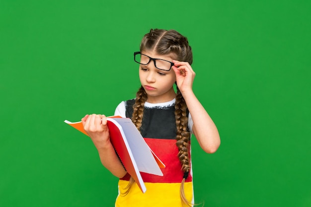 A thoughtful child with a German flag and a notebook in his hands on a green isolated background German language courses for schoolchildren