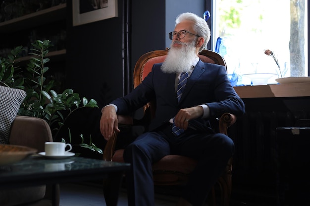 Thoughtful confident handsome businessman thinking while sitting on armchair in his modern office about business concept