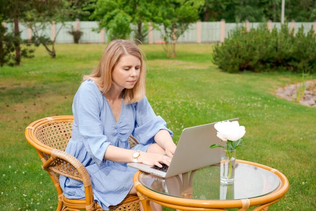 공원이나 정원에 있는 테이블에서 노트북으로 일하는 사려 깊은 귀여운 여성