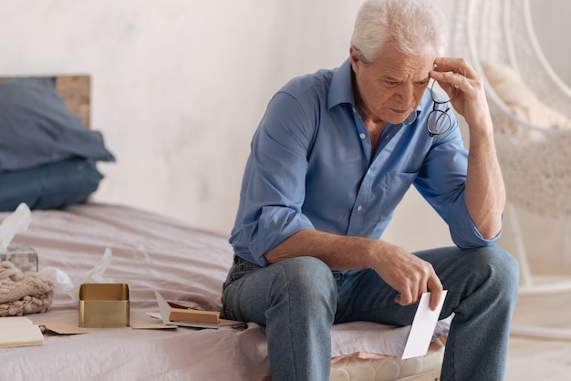 Thoughtful depressed unhappy man holding a letter and touching his head while being involved in his memories