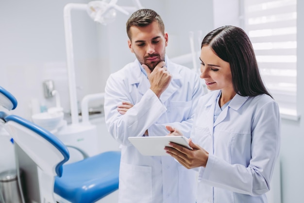 Thoughtful doctor and assistant looking at digital tablet screen in modern dental clinic