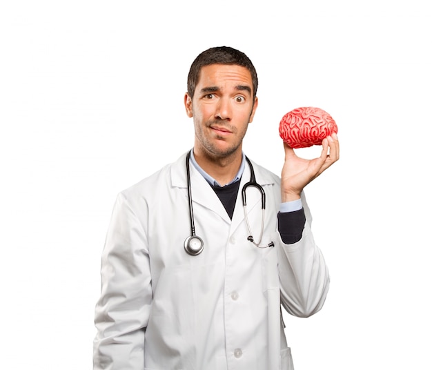 Thoughtful doctor holding a toy brain against white background