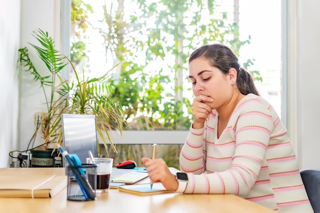 Thoughtful entrepreneur making notes while working on laptop in home office