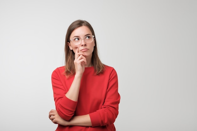 Thoughtful european woman in red sweater is looking up thinking or planning