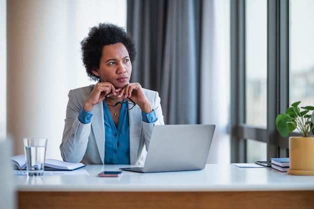 Photo thoughtful female executive looking away while working on laptop at office desk