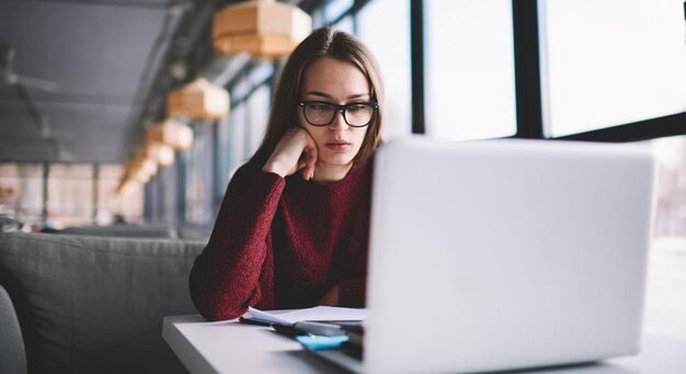 Thoughtful female student it developer learning at college library while watching interesting movie