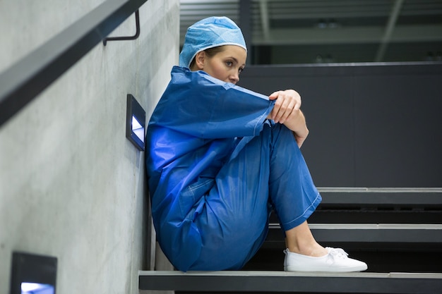 Thoughtful female surgeon sitting on staircase