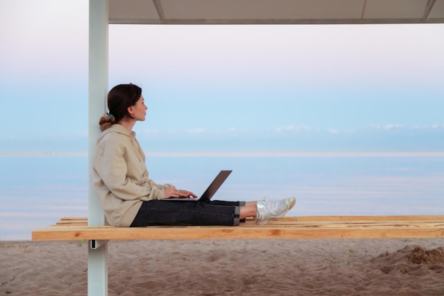 Thoughtful freelance woman sitting on beach bench looking at beautiful lake