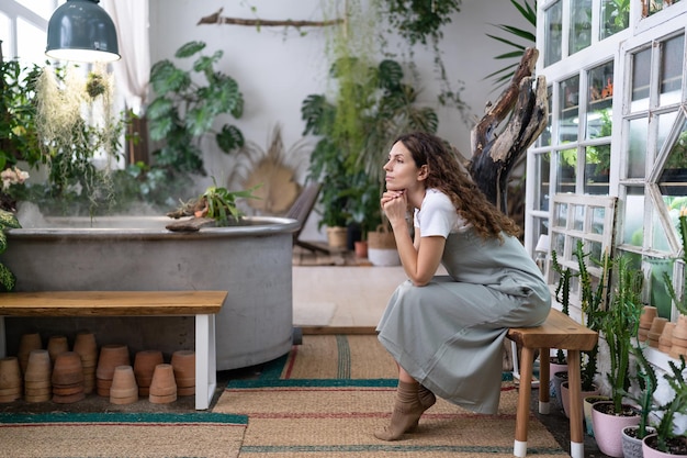 Thoughtful gardener female resting after work in floral store or greenhouse mental health concept