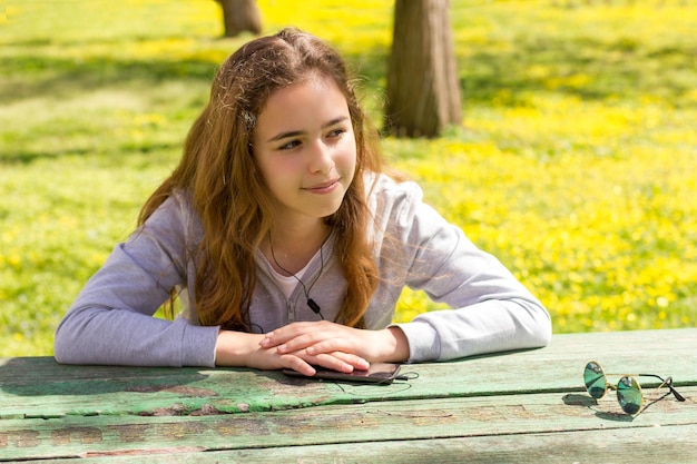 Photo thoughtful girl listening music while sitting at table in park