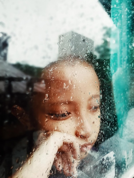 Photo thoughtful girl seen through wet glass window