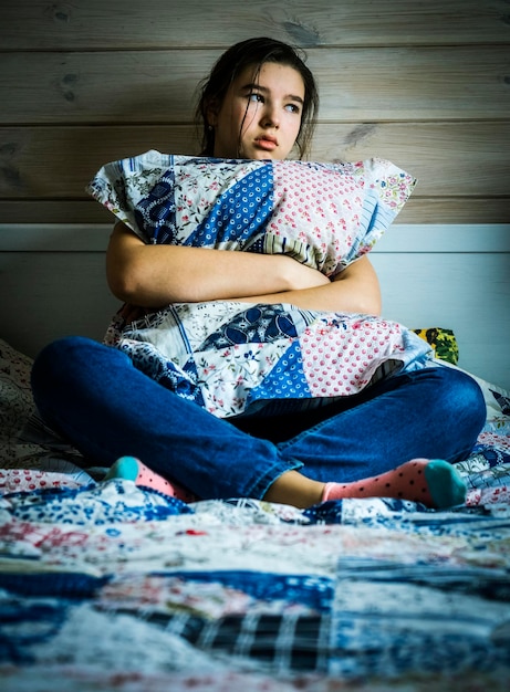 thoughtful girl sitting on bed at home