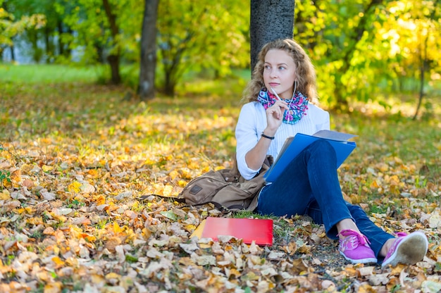 Thoughtful girl student sits and writes in the autumn park